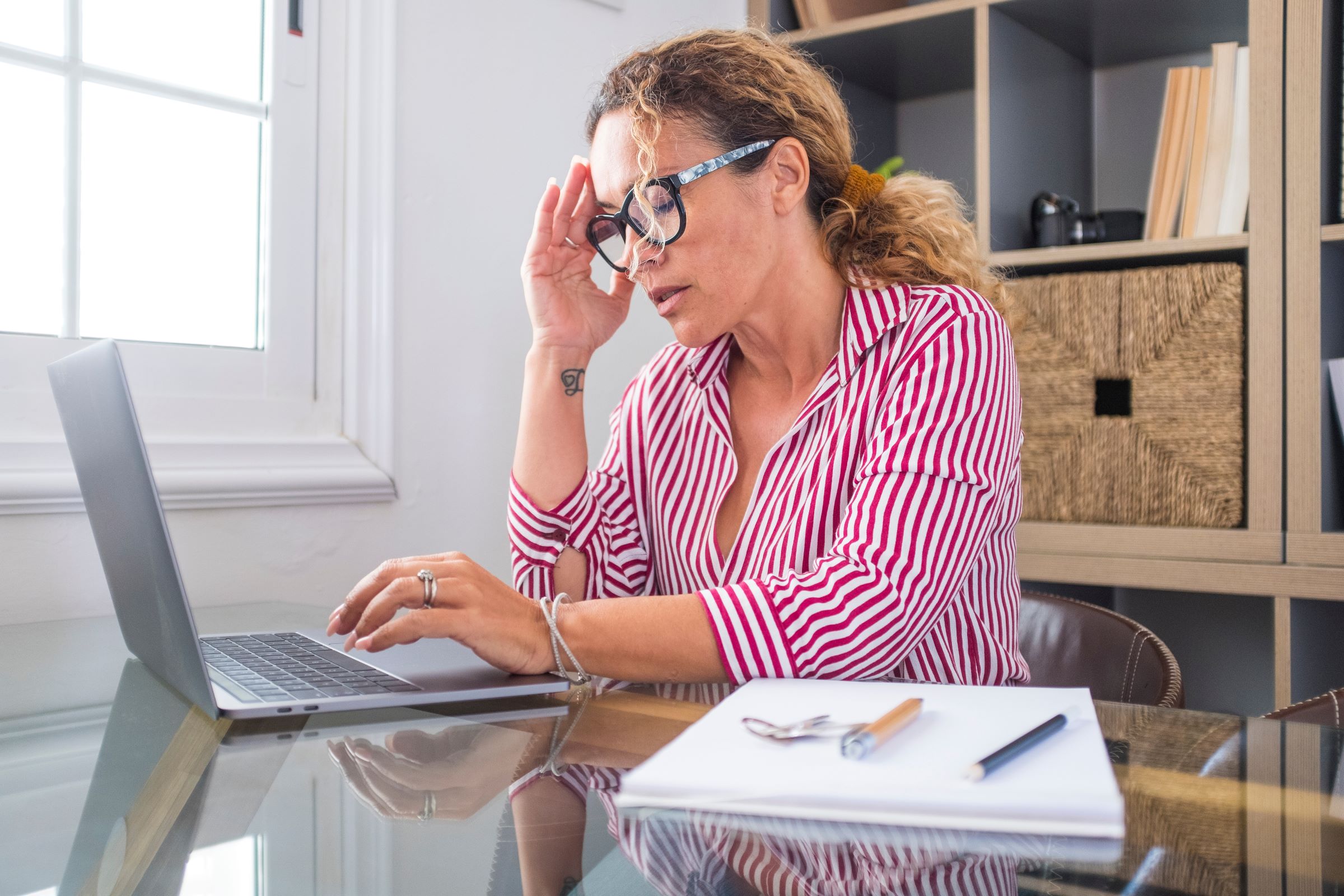 Woman holds head feeling stressed while working in home office with laptop.