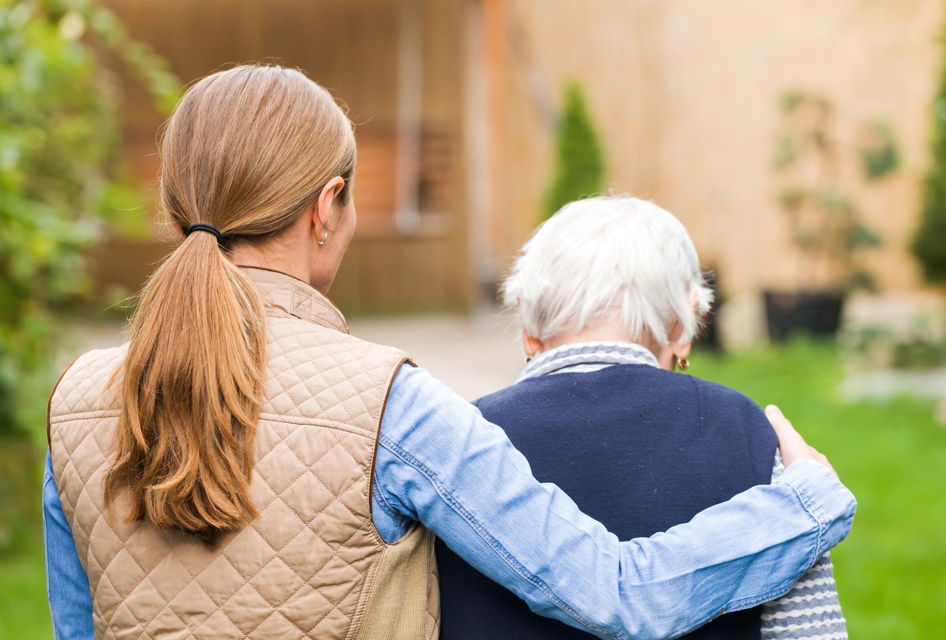 Adult daughter walks with her arm around her senior mother outside